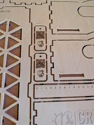 Close-up of the cut sheet showing tab joinery, a triangle-pattern panel and engraved QR-code tags
