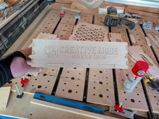 Project box side panel engraved with the Creative Mode Arts & Play Centre logo, held over the CNC table